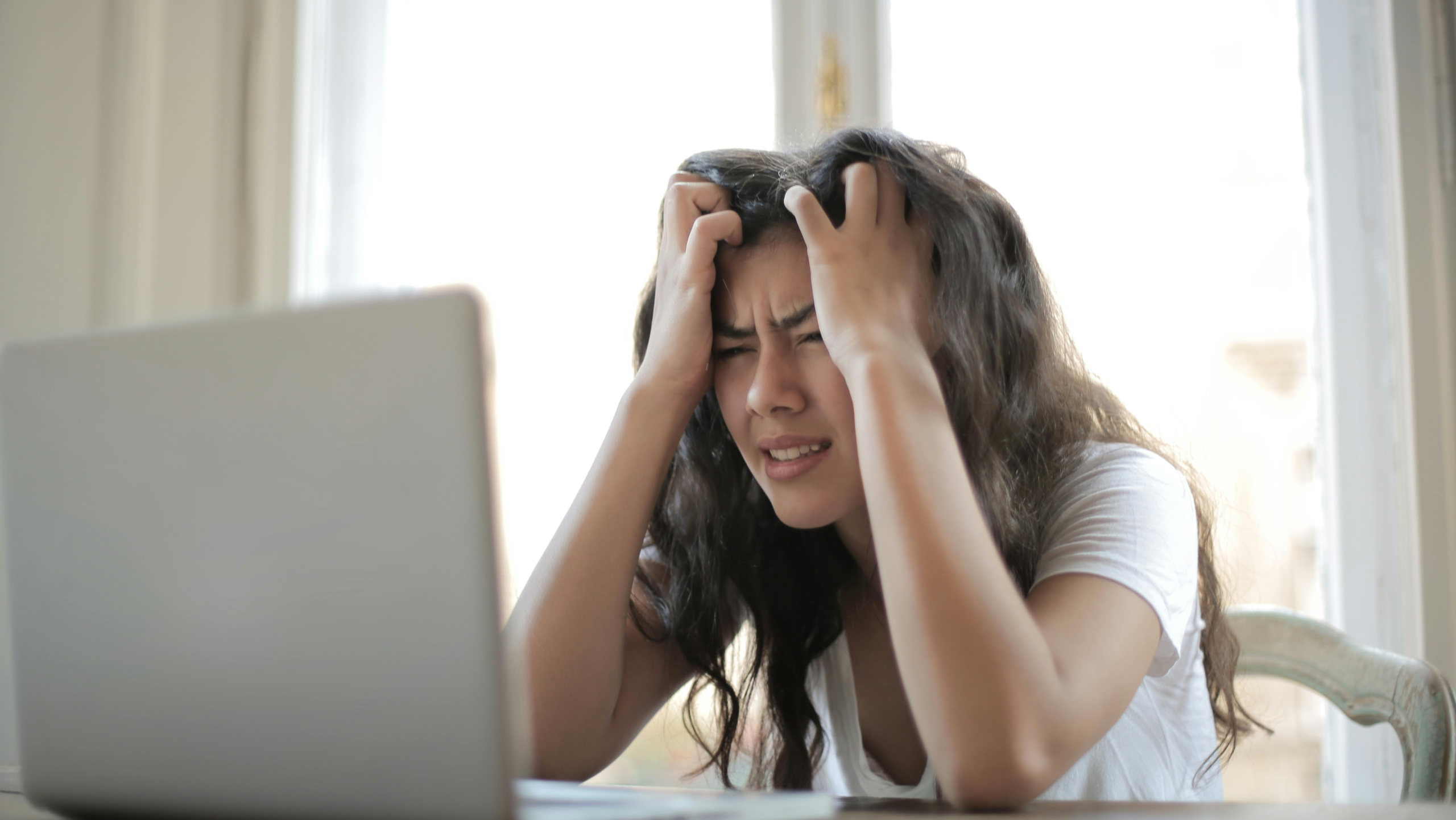 mulher em frente ao computador preocupada, com as mãos na cabeça, porque estuda demais, mas não aprende